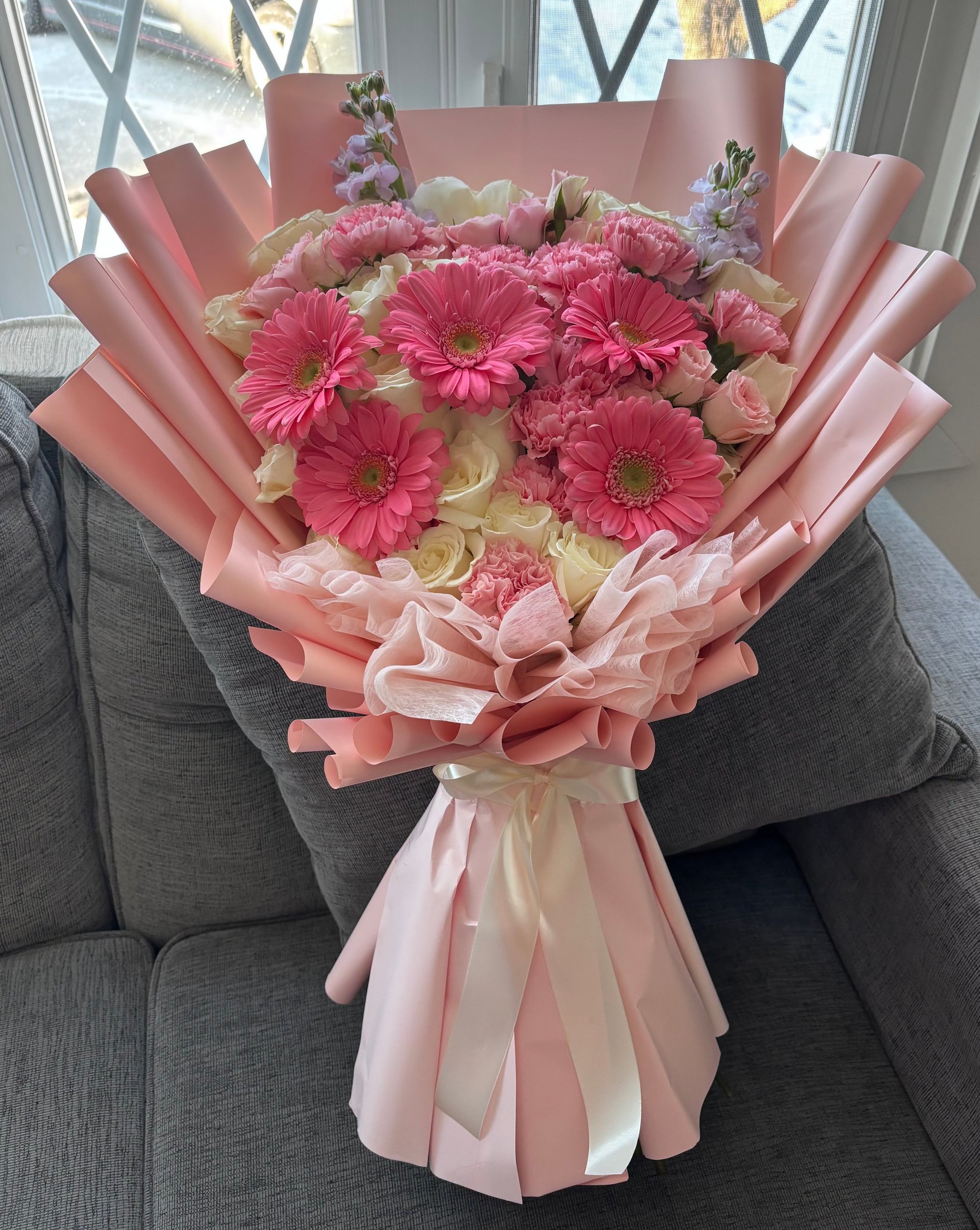 Pink floral bouquet with hot pink gerberas on gray couch