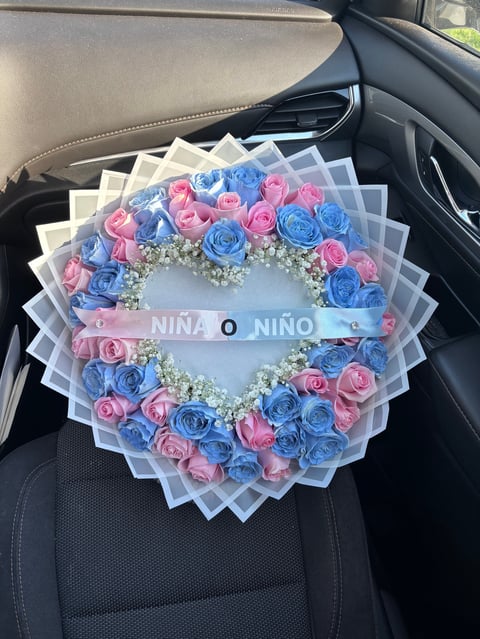 Heart-shaped floral wreath with pink and blue roses and babys breath in car seat, displaying Nino O Nino gender reveal message
