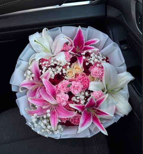 Luxurious bouquet of pink lilies, roses, carnations, and babys breath wrapped in white tissue paper on a car seat