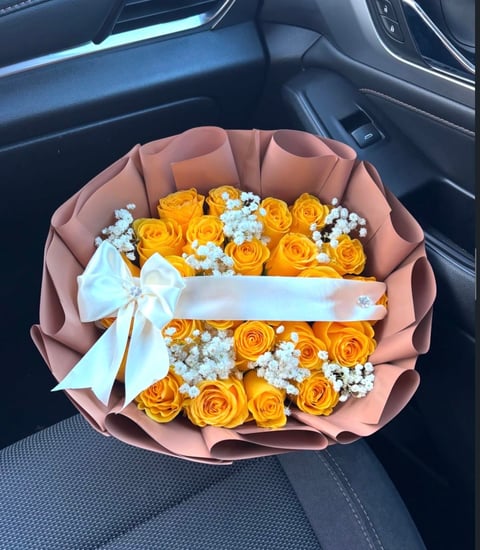 Bouquet of yellow roses and white babys breath wrapped in blush pink paper with white ribbon, placed in a car seat
