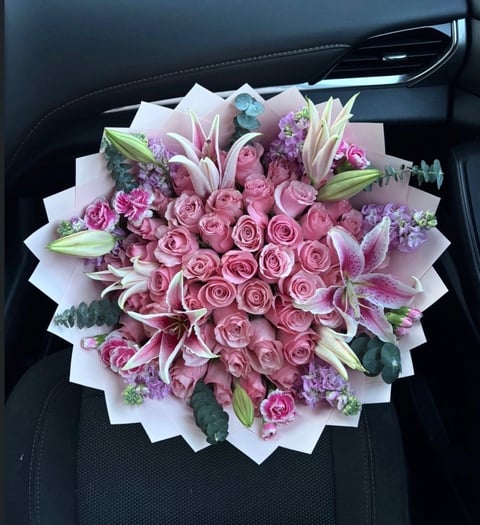 Luxurious bouquet of pink roses and lilies wrapped in white tissue paper, displayed on car seat
