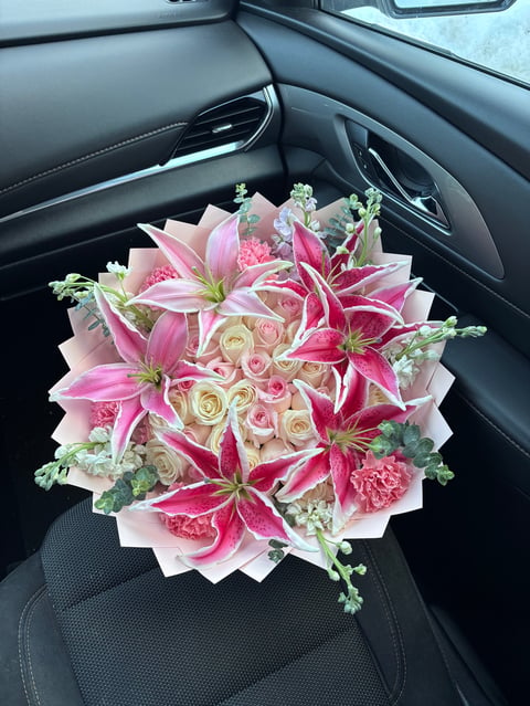 Luxurious bouquet of pink lilies, roses, and carnations with greenery arranged on a car seat