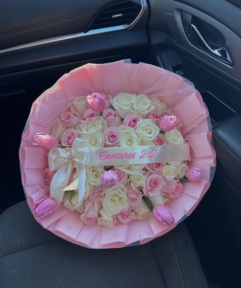 Luxurious bouquet of pink and white roses wrapped in pink paper with white bow, placed in car seat