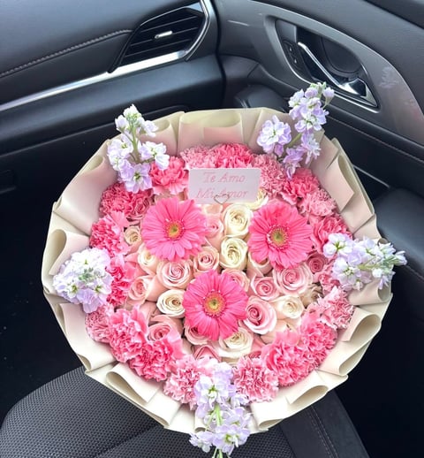 Large bouquet of pink roses, carnations, and white flowers wrapped in cream paper on a car seat